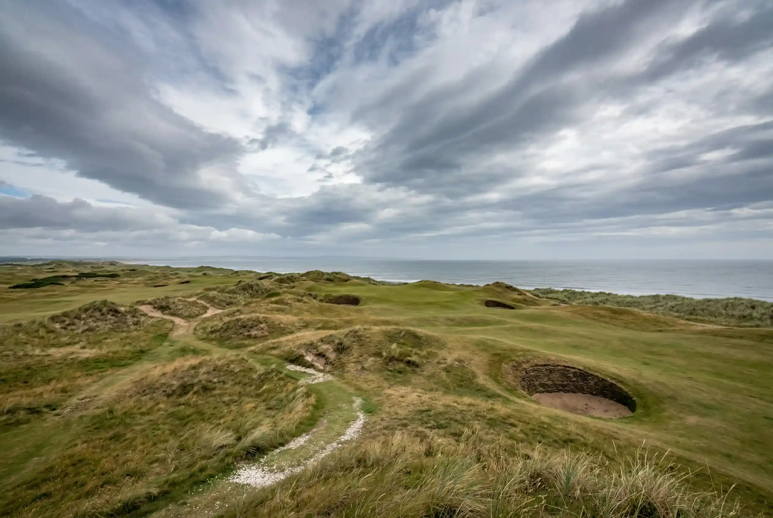 Campo de links escocés junto al mar con bunkers de arena y cielo con nubes de tormenta